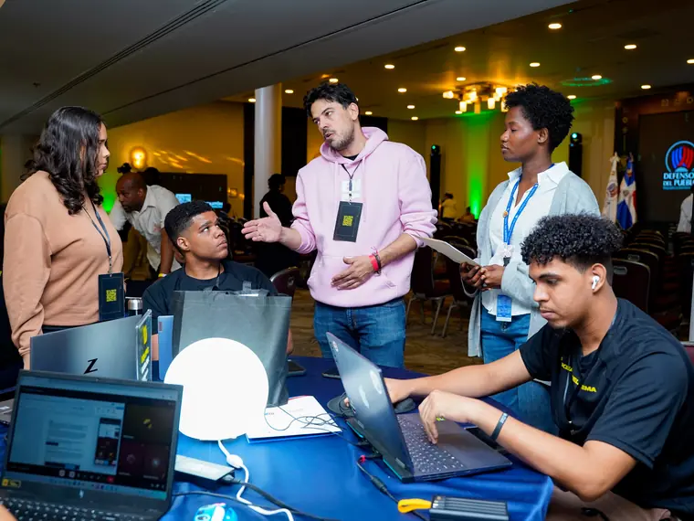 Un grupo de participantes trabaja en computadoras portátiles alrededor de una mesa durante un hackatón