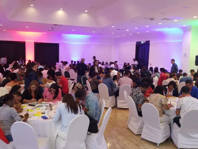 Salón amplio con mesas redondas ocupadas por decenas de participantes durante una actividad de trabajo en grupo