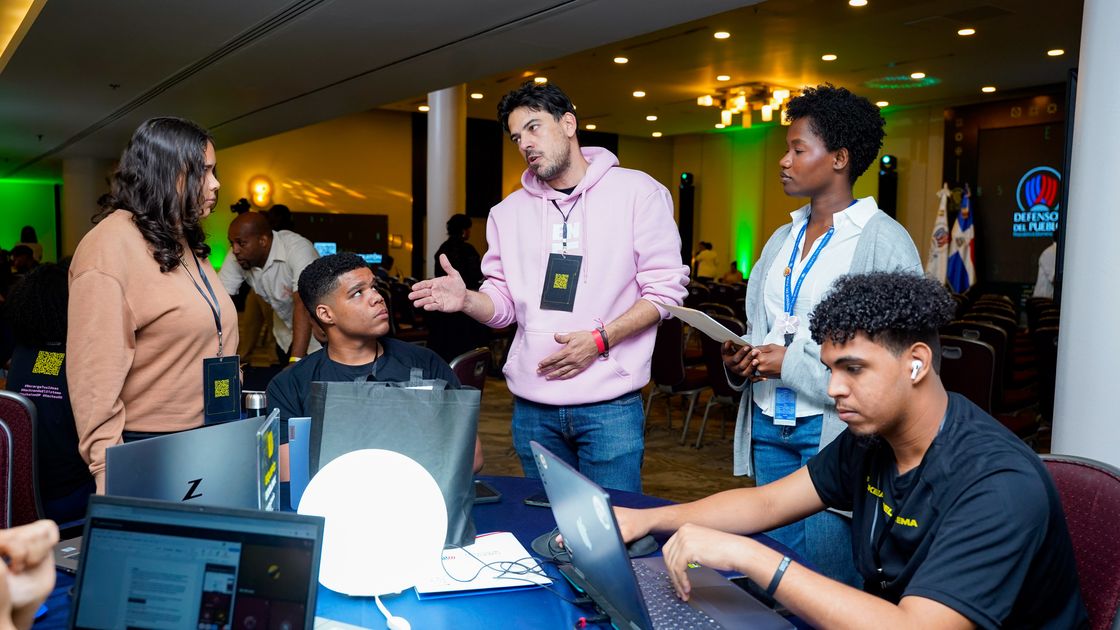 Un facilitador de Fundación Enlata acompaña a un equipo de jóvenes frente a sus laptops durante un hackatón.