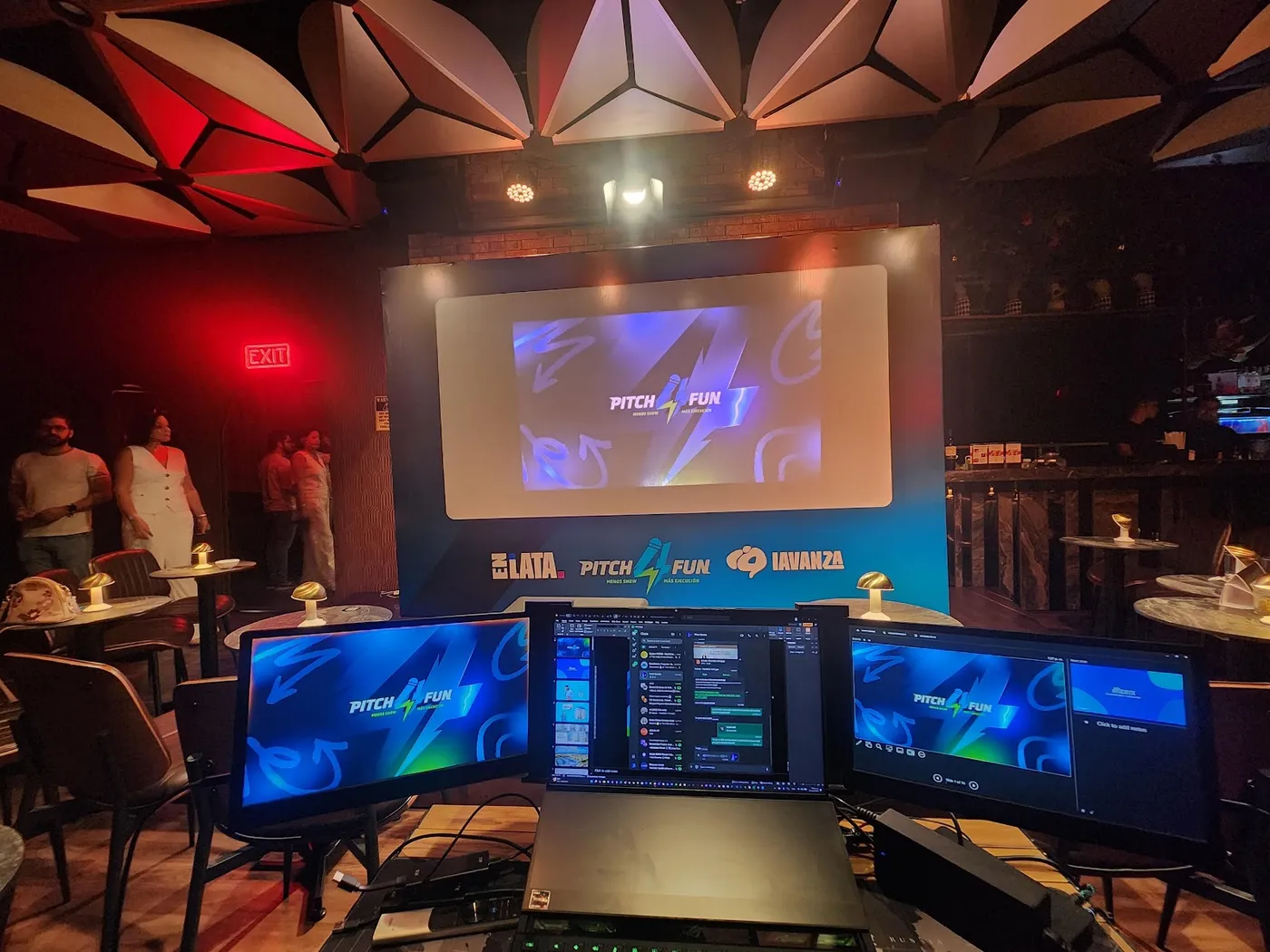 Puesto técnico con varios monitores y el escenario del evento al fondo